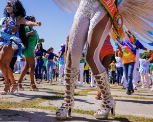 Festividade de carnaval, com pessoas dançando. Em primeiro plano, aparecem as pernas de um passista
