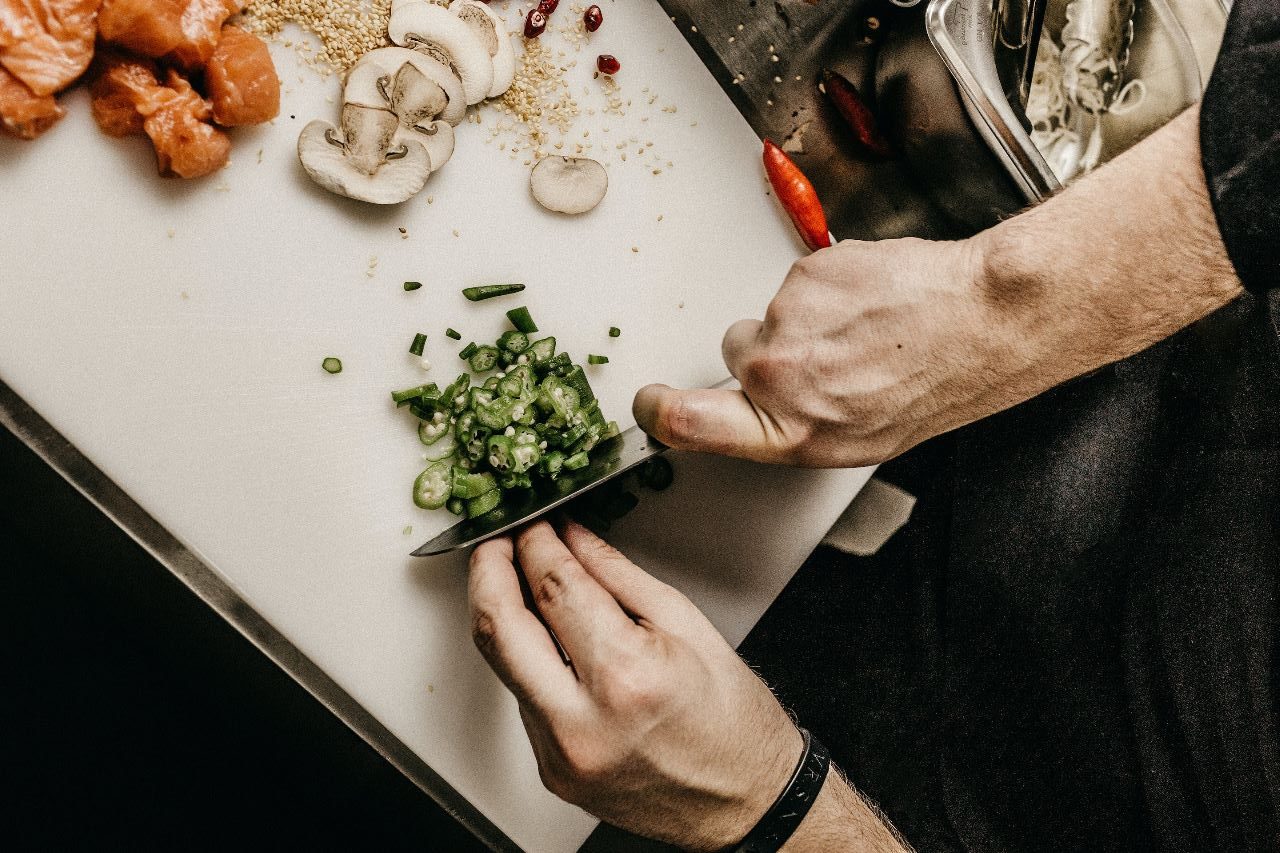 Mãos cortando alimentos diversos como quiabos e cogumelos