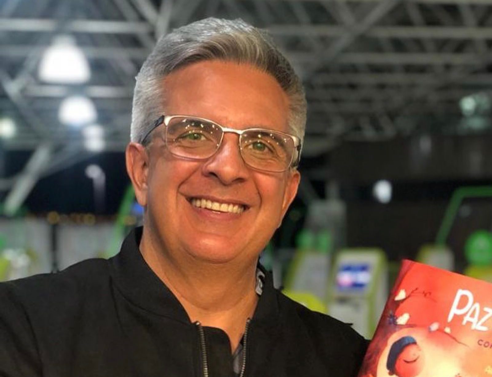 Homem de óculos e cabelo grisalho sorri e mostra livro