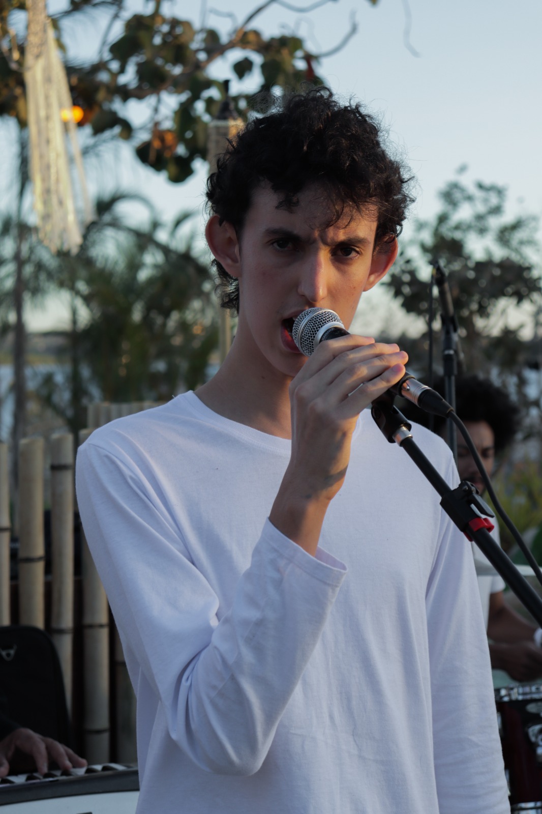 Jovem de camiseta branca, canta ao microfone