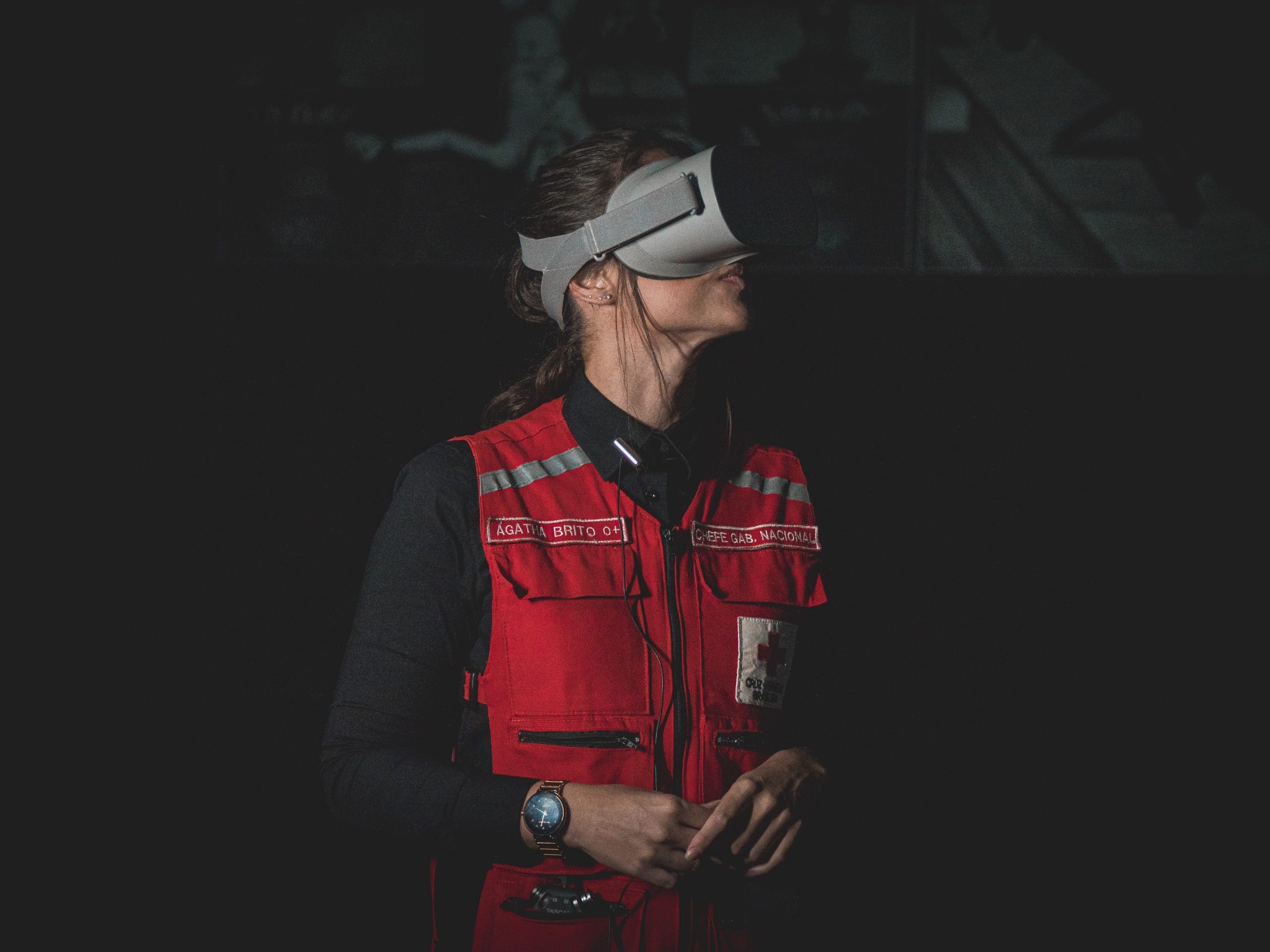 Mulher com colete vermelho, de perfil, usa óculos de realidade virtual