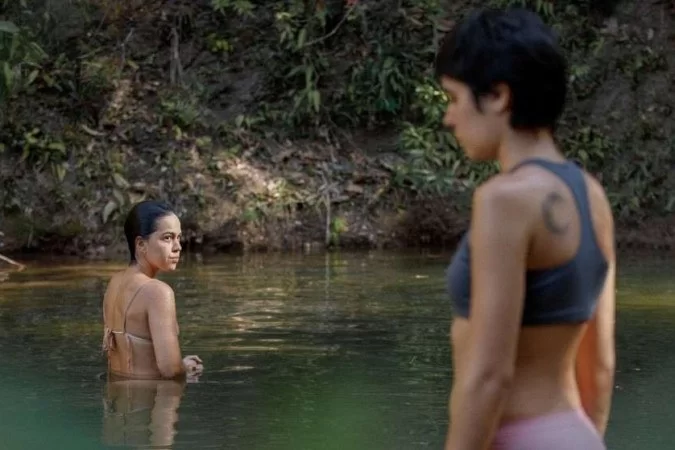 Protagonistas do curta As Miçangas em cena realizada num rio, uma em frente da outra de biquini