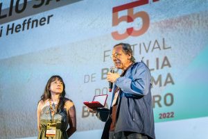 No palco do Cine Brasília, Hernani Heffner segura prêmio ao lado de Sara Rocha