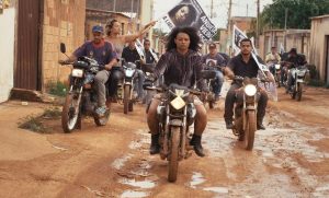 Frame do filme Mato Seco, com pessoas em roupas pretas dirigem motos em rua de terra