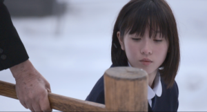 Trecho do filme Mochi, mostra uma mulher japonesa olhando uma espécie de martelo de madeira